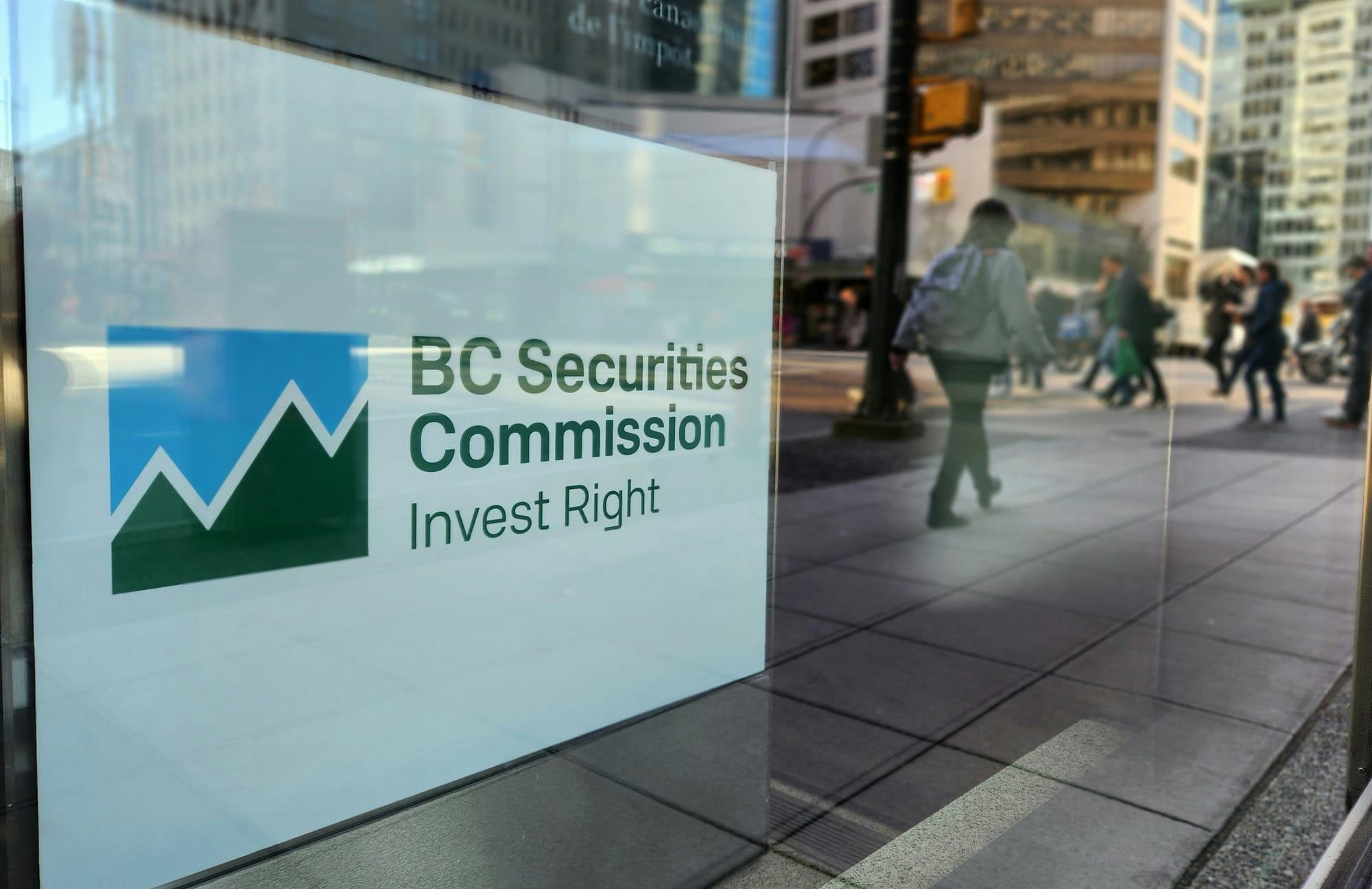 A sign reading 'B.C. Securities Commission: Invest Right' sits in a window as pedestrians walk by.