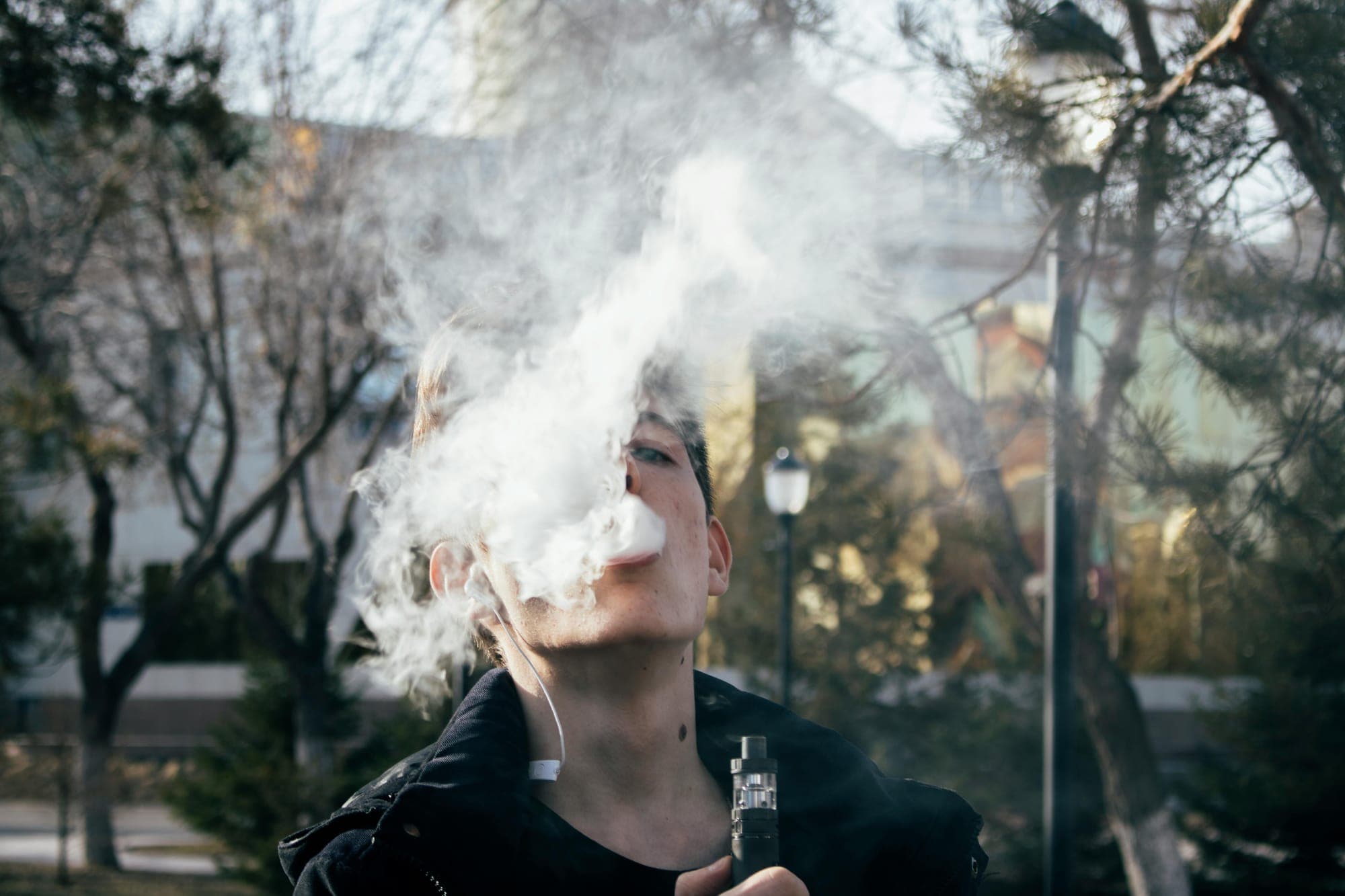 A young man blows a cloud of vape smoke so his face is mostly obscured